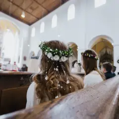 Dwie dziewczynki w wiankach siedzą w kościele podczas komunii.