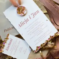 Eleganckie zaproszenia ślubne z ozdobnymi piórami i złotymi elementami.
