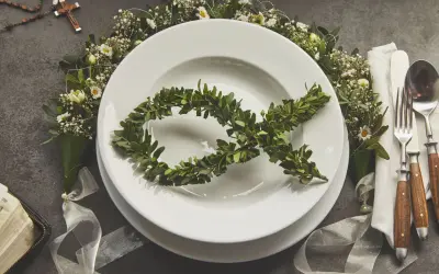 Eleganckie menu na komunię w domu. Na talerzu symbol ryby z gałązek, wokół kwiaty i różaniec.