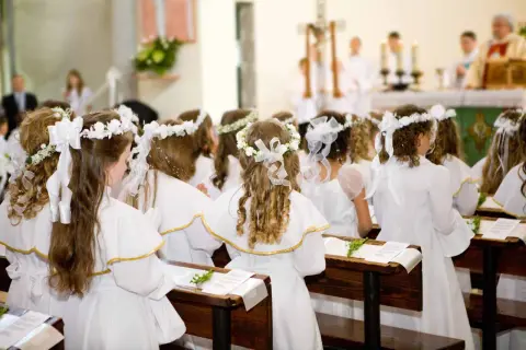 Dzieci w białych strojach, z wiankami na głowach, siedzą w ławkach kościoła. To uroczysty biały tydzień, czas pierwszej komunii świętej.