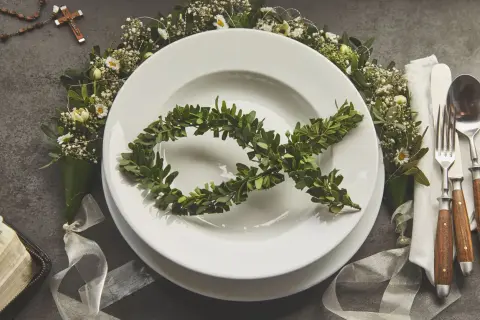 Eleganckie menu na komunię w domu. Na talerzu symbol ryby z gałązek, wokół kwiaty i różaniec.