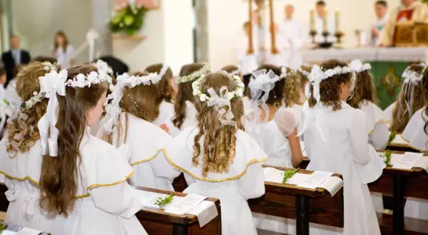 Dzieci w białych strojach, z wiankami na głowach, siedzą w ławkach kościoła. To uroczysty biały tydzień, czas pierwszej komunii świętej.