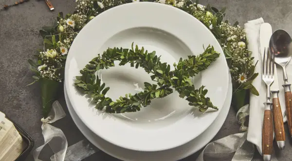Eleganckie menu na komunię w domu. Na talerzu symbol ryby z gałązek, wokół kwiaty i różaniec.