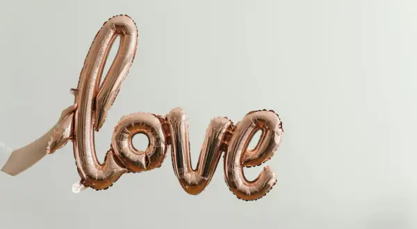 Różowe balony w kształcie napisu "love" unoszą się w powietrzu, symbolizując bezwarunkową miłość do dziecka. Cytaty o tej miłości pasują do tej chwili.