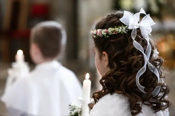 Dziewczynka z wiankiem i kokardą na głowie, trzymająca świecę. W tle chłopiec w białej komży. Biały tydzień po komunii.
