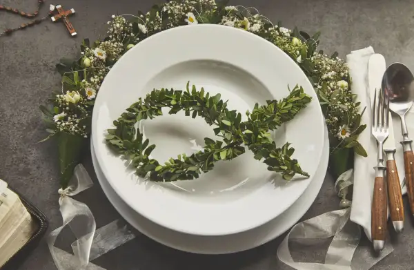 Eleganckie menu na komunię w domu. Na talerzu symbol ryby z gałązek, wokół kwiaty i różaniec.
