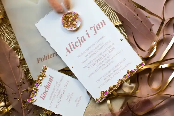 Eleganckie zaproszenia ślubne z ozdobnymi piórami i złotymi elementami.