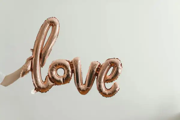 Różowe balony w kształcie napisu "love" unoszą się w powietrzu, symbolizując bezwarunkową miłość do dziecka. Cytaty o tej miłości pasują do tej chwili.